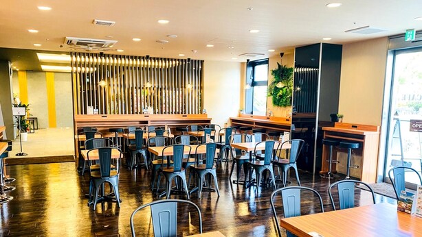 A modern restaurant interior with wooden tables and chairs, a central bar area, and a decorative vertical panel.