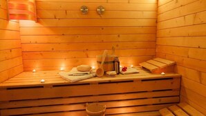 Eine Holzsauna mit Bänken, Kerzen, Handtüchern und einem Eimer.