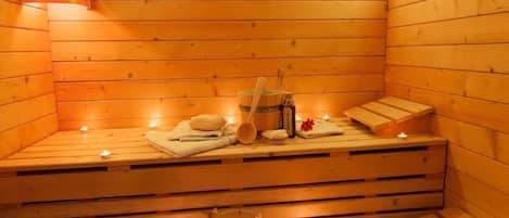 Una sauna de madera con bancos, velas, toallas y un cubo.