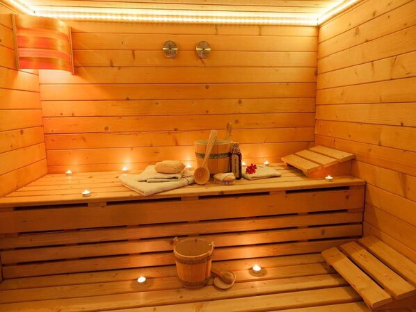 Una sauna de madera con bancos, velas, toallas y un cubo.