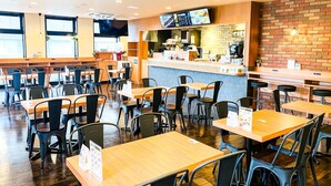 Ein Restaurantinneres mit Holztischen und -stühlen, einer Theke mit Speisekarten und einer Ziegelwand.