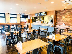 A restaurant interior with wooden tables and chairs, a counter with a menu display, and a brick wall. - Hotel Livemax Premium Nagano Ekimae (Nagano)