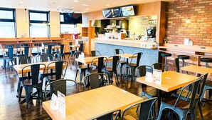 A restaurant interior with wooden tables and chairs, a counter with a menu display, and a brick wall.