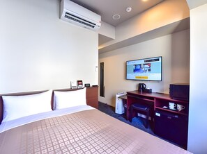 Una habitación de hotel con cama, escritorio, televisión y aire acondicionado.