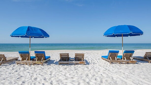 A beach with wooden lounge chairs and blue umbrellas. - Two Bedroom, Ocean Front, Luxury Condo, Panama City Beach, Florida 4253341 (Panama City Beach)