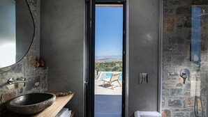 Un baño moderno con un lavabo de piedra, un espejo grande y una ducha con paredes de piedra.
