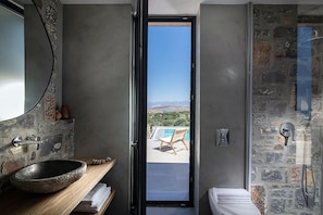A modern bathroom with a stone sink, a large mirror, and a shower with stone walls. - Ninemia Villa III in Crete (Plaka)
