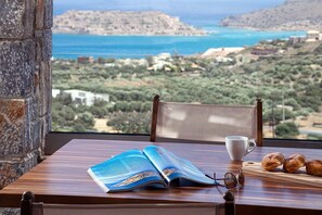 A wooden table with a book, a cup, and pastries, overlooking a coastal landscape. - Ninemia Villa III in Crete (Plaka)