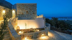 A stone building with a flat roof and a small garden area, overlooking a coastal landscape. - Ninemia Villa III in Crete (Plaka)