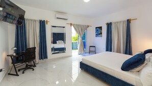 Un dormitorio con una cama grande, un escritorio y una silla. Hay una ventana con cortinas, un equipo de aire acondicionado y un cuadro en la pared.