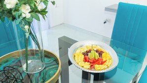 Una mesa de cristal con un frutero y un jarrón con flores blancas.