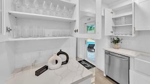 Una cocina moderna con armarios blancos, lavavajillas integrado y una encimera con tetera y teléfono.