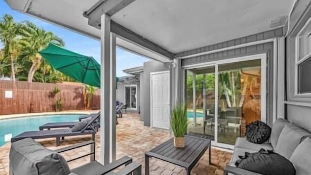 Un patio cubierto con piscina, mobiliario exterior y una puerta corrediza de vidrio que da a un jardín trasero.