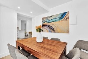 A dining area with a wooden table, grey chairs, and a large abstract painting on the wall. - Sunny Days Getaway, 5BD Heated Pool Family Home! (Fort Lauderdale)