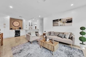 A modern living room with a sofa, coffee table, and a clock on the wall. - Sunny Days Getaway, 5BD Heated Pool Family Home! (Fort Lauderdale)