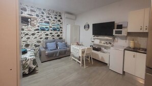 A compact living space with a stone wall, a sofa, a dining table, a TV, and a kitchenette. - Noda House Tarajalejo (Tarajalejo)