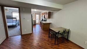 A spacious room with hardwood flooring, a dining table with chairs, a kitchen area with cabinets and appliances, and a doorway leading to another room. - North Liberty Townhouse (North Liberty)
