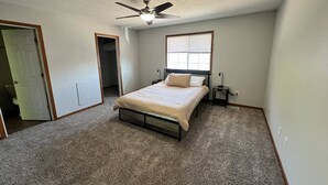 A bedroom with a bed, a ceiling fan, a window, and a door. - North Liberty Townhouse (North Liberty)
