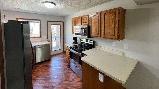 A kitchen with wooden cabinets, a stainless steel refrigerator, a dishwasher, a stove, and a microwave. - North Liberty Townhouse (North Liberty)