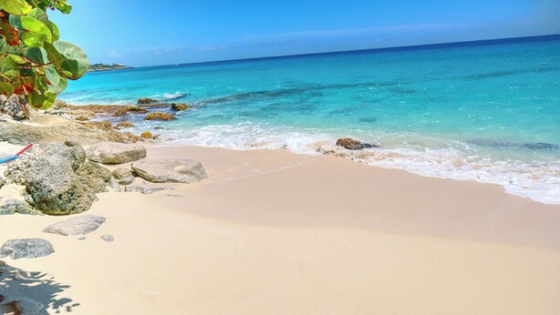 A beach with clear turquoise water, sandy shore, and large rocks. - Sapphire Beachfront Penthouse (Lowlands)