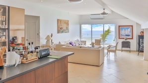 A spacious living area with a large island, a sofa, and a view of the ocean. There is a kitchen area with a counter and various appliances. - Sapphire Beachfront Penthouse (Lowlands)