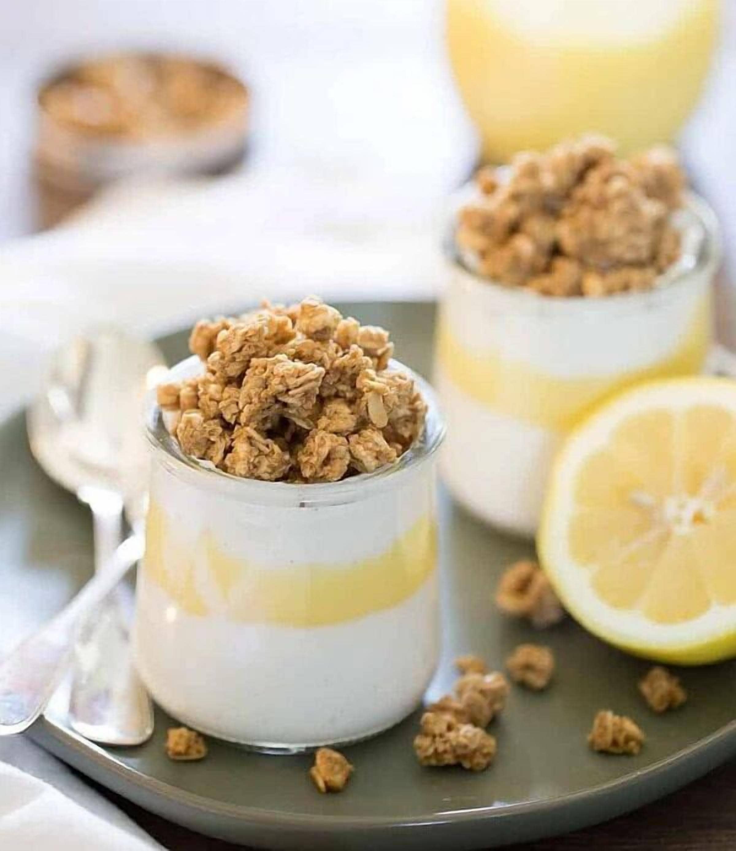 Drei Gläser Joghurt mit Granola und Zitronenscheiben auf einem Teller.