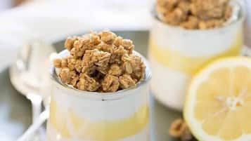 Drei Gläser Joghurt mit Granola und Zitronenscheiben auf einem Teller.