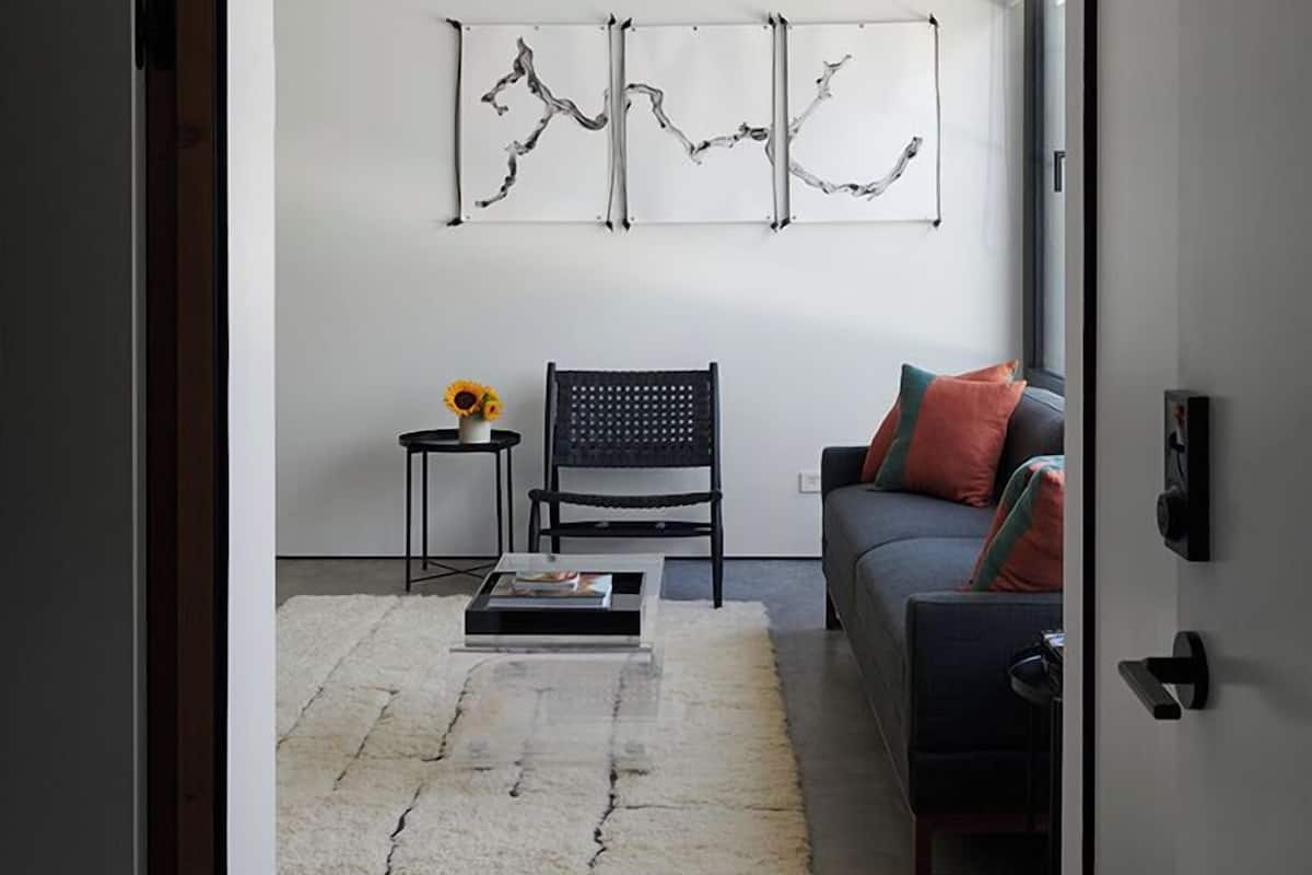 A modern living room with a sofa, a black chair, a small table with a vase, and abstract wall art.