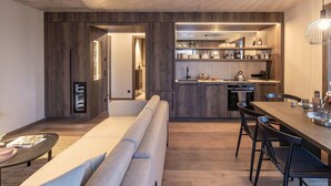 Una cucina moderna con mobili in legno, un'area pranzo con un tavolo lungo e sedie, e un angolo salotto accogliente con una panca.