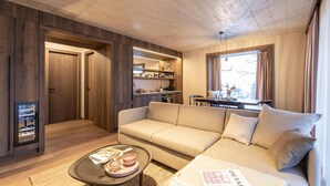 Un soggiorno moderno con un divano, un tavolino e una cucina visibile attraverso una porta aperta.