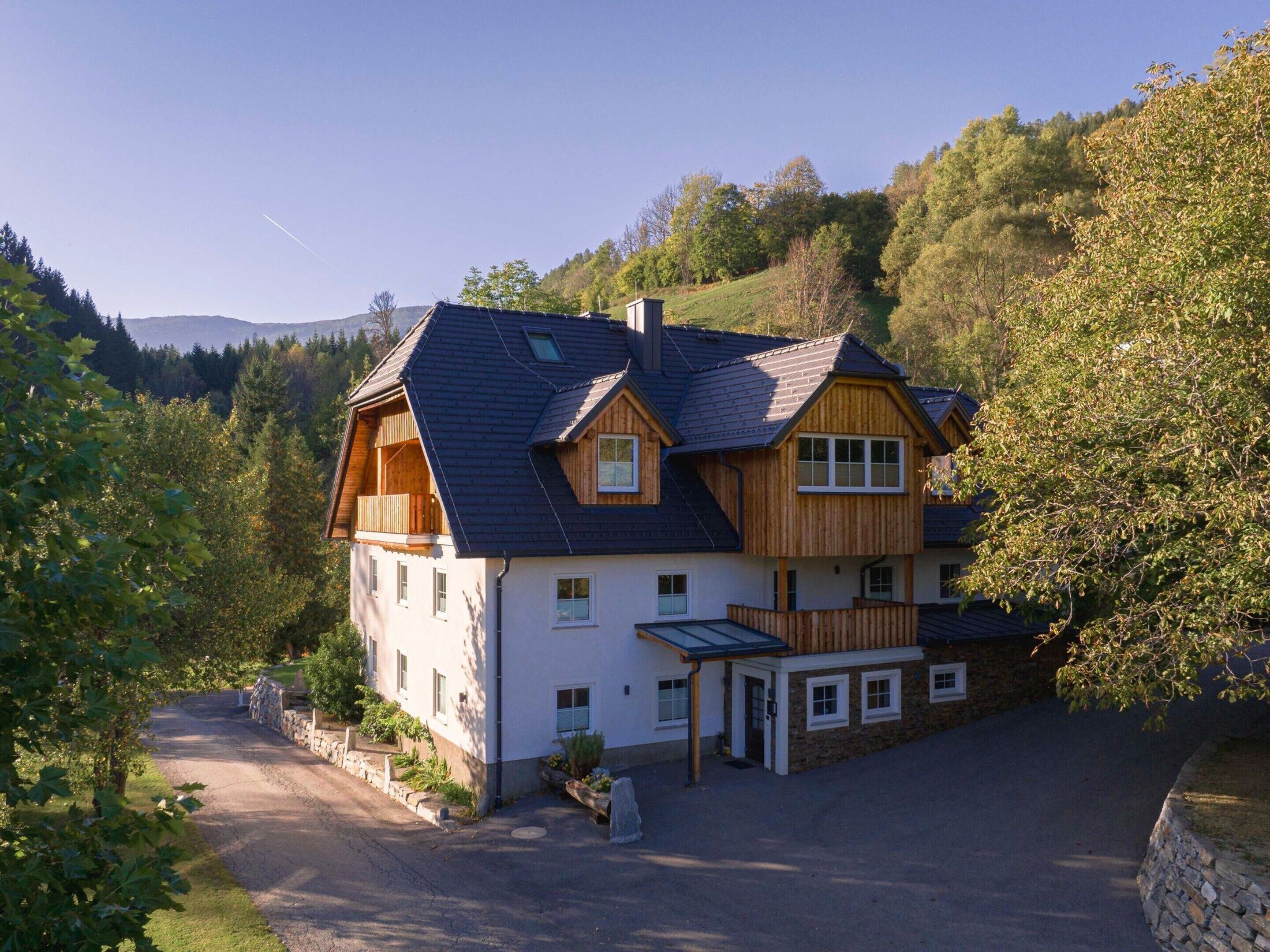 Ein großes, zweistöckiges Haus mit einem geneigten Dach, einem Balkon und einer Steinmauer, die das Grundstück umgibt.