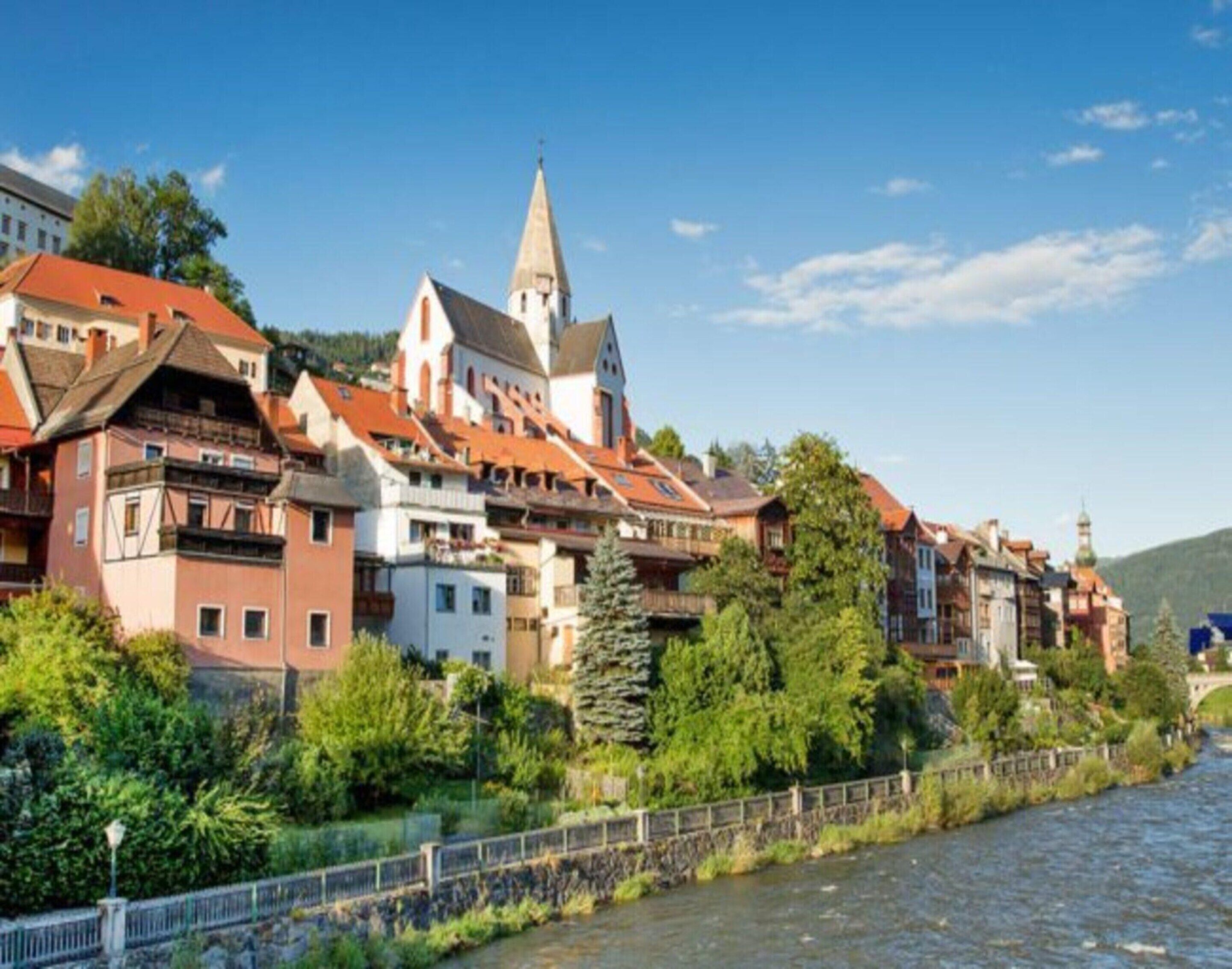 Un pueblo a orillas del río con arquitectura europea tradicional, que incluye una iglesia con un campanario alto.