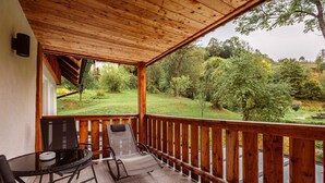 A covered balcony with a wooden railing, a table with chairs, and a view of a green landscape. - Holiday Apartment on Kreischberg (Sankt Georgen am Kreischberg)