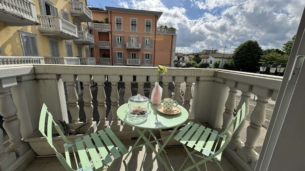 A balcony with a table and chairs, a vase with flowers, and a view of multi-story buildings. - Charming Tuscan Home With Pool Near Lucca (Lucca)