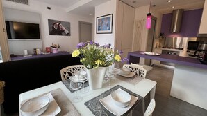A modern kitchen with a central island, a dining area with a white table set for four, and a flat-screen TV mounted on the wall. - Charming Tuscan Home With Pool Near Lucca (Lucca)