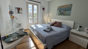 A bedroom with a bed, bedside table, and a window with a view of buildings. - Charming Tuscan Home With Pool Near Lucca (Lucca)
