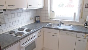 A kitchen with white cabinets, a stove, an oven, a sink, and a window. - Haus in Nessmersiel am Wattenmeer (Dornum)