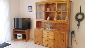 A living room with a wooden cabinet, a television, and a fireplace. - Haus in Nessmersiel am Wattenmeer (Dornum)
