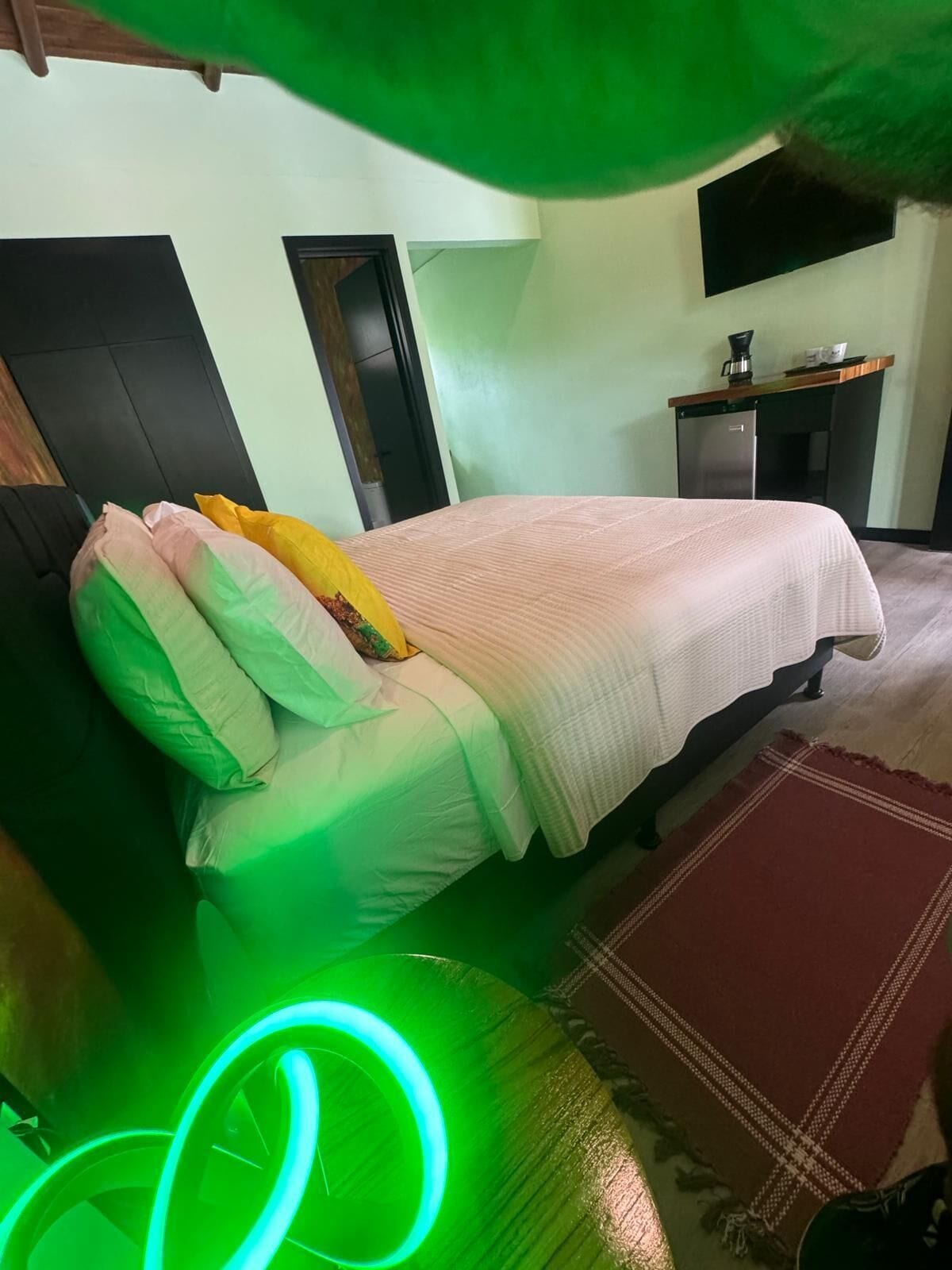 A hotel room with a bed, a desk, and a green neon light.