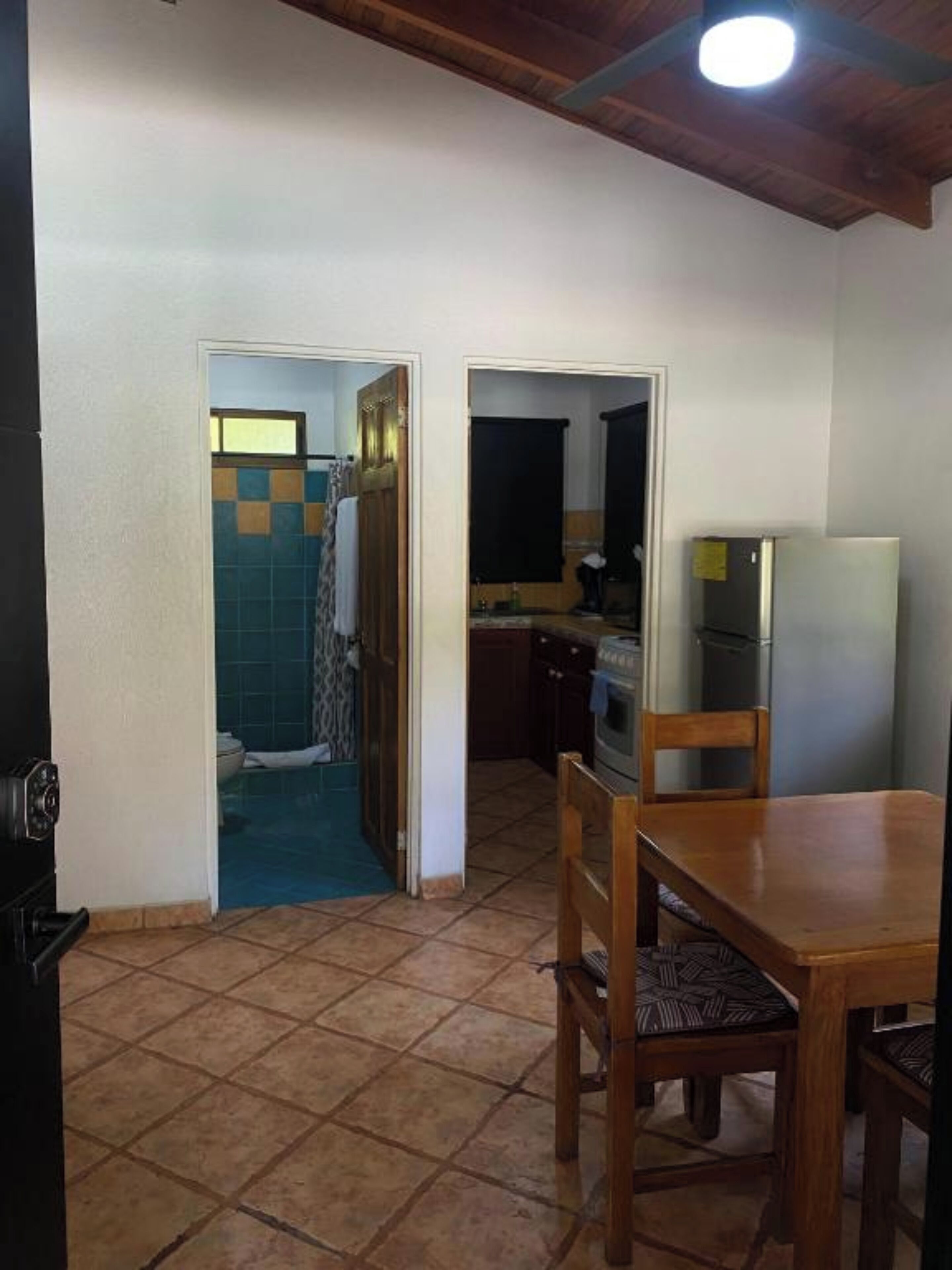 A compact kitchen with a dining area, a tiled floor, and a wooden ceiling.