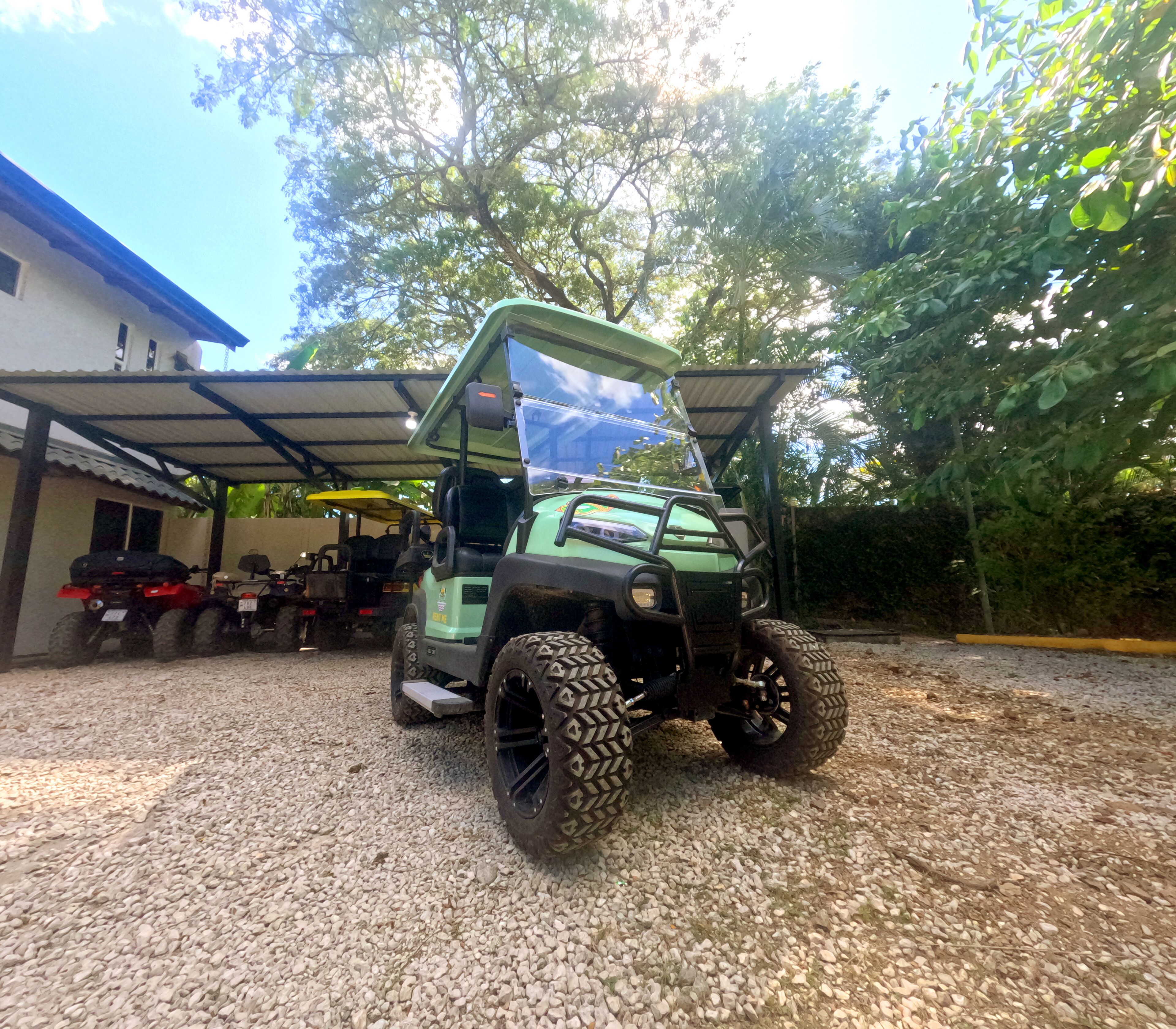 A green golf cart parked on gravel with a covered area in the background.