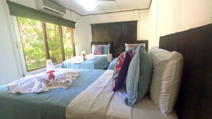 A hotel room with two beds, a ceiling fan, and a window with a view of greenery. - Parti Gras Hotel & Villas en Potrero (Tempate)