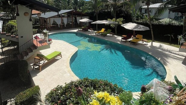 A pool area with lounge chairs and umbrellas, surrounded by tropical plants and palm trees. - Parti Gras Hotel & Villas en Potrero (Tempate)
