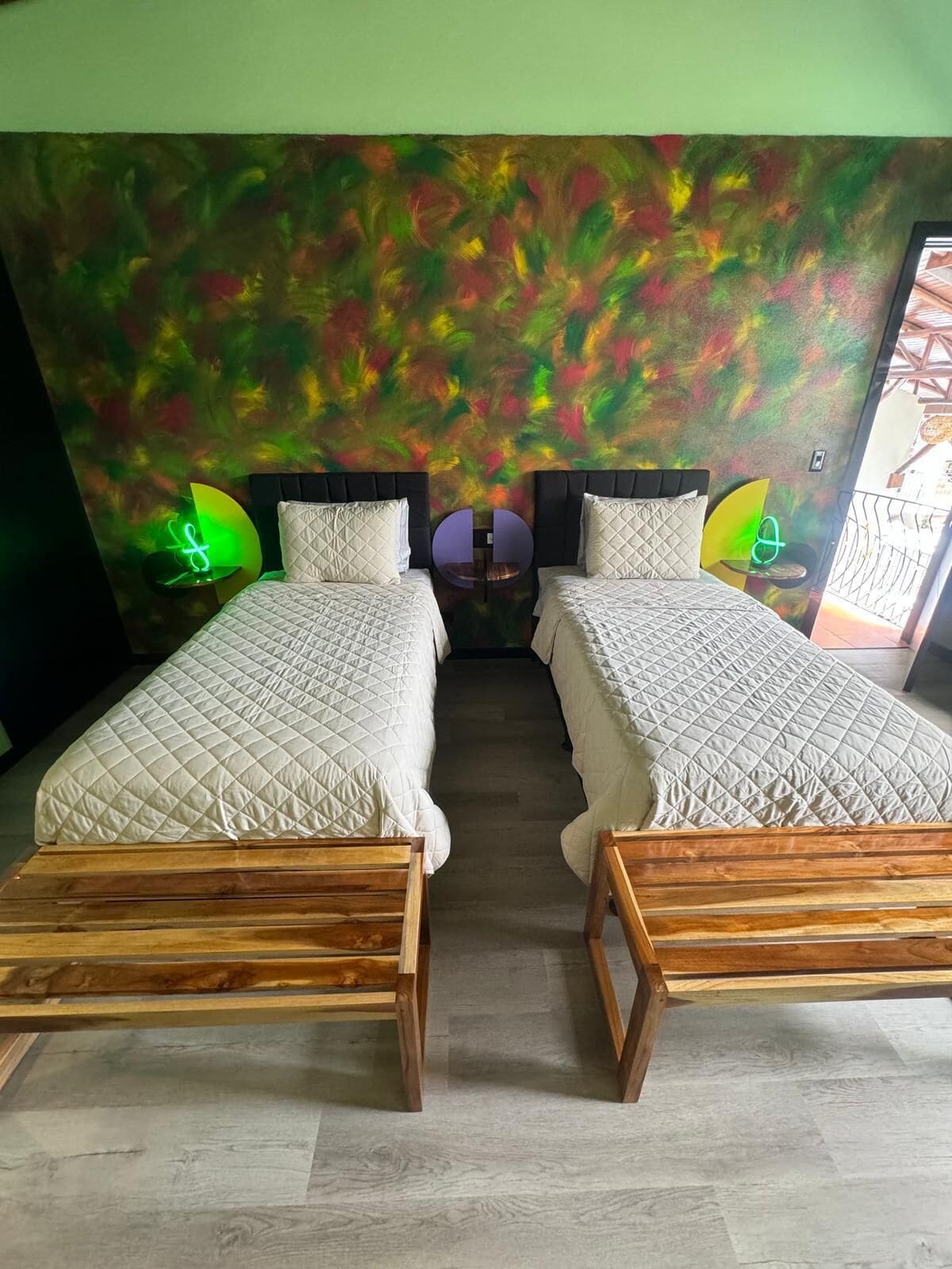 Ein Zimmer mit zwei Betten, einem runden Tisch und einer farbenfrohen, abstrakten Wand.