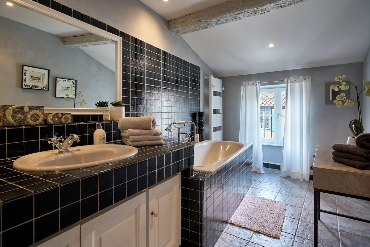 Un baño con salpicadero de azulejos negros, un espejo grande, lavabo doble y bañera.
