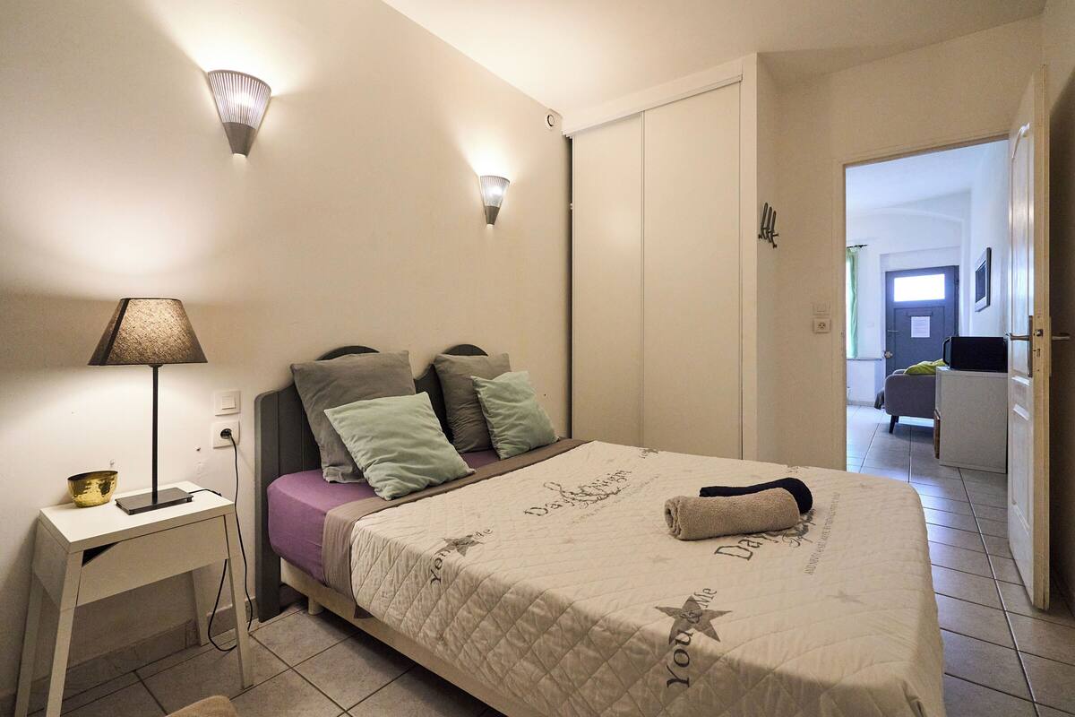 Un dormitorio con cama, mesita de noche, lámpara y una puerta que da a otra habitación.