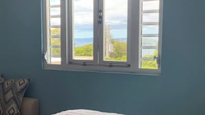 Une chambre à coucher avec un lit, une fenêtre et une vue sur la verdure et un bâtiment.