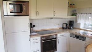 A compact kitchen with white cabinets, a built-in microwave, a stove, and a coffee maker. - Allergiker Freundliches Haus in Nessmersiel (Dornum)