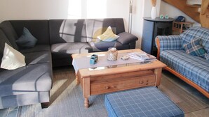 Un salon comprenant un canapé, une table basse, un plaid, un meuble en bois et un escalier.