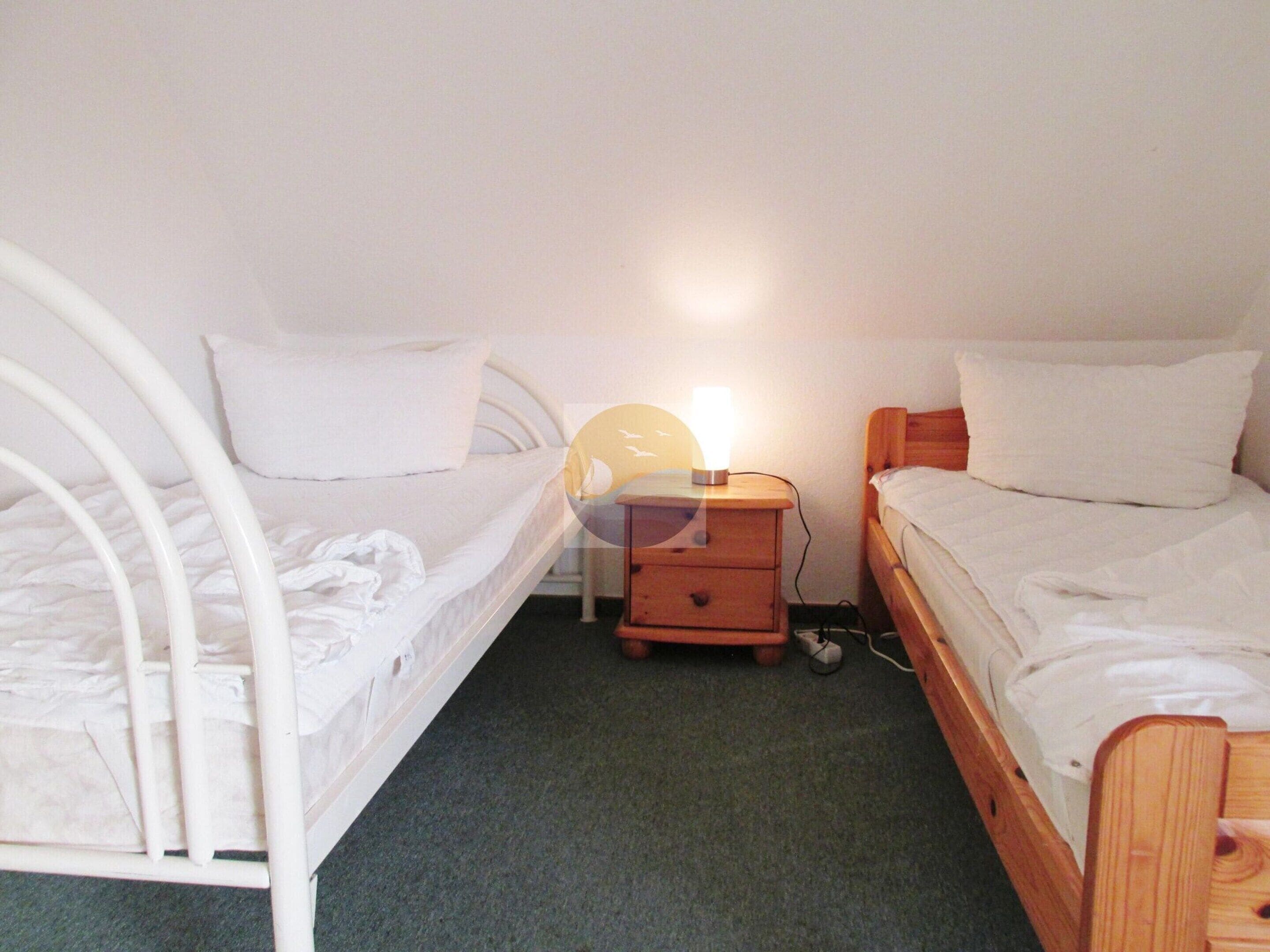 A bedroom with two single beds, a wooden nightstand with a lamp, and a carpeted floor.